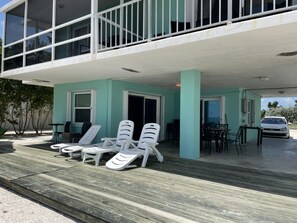 A building with a covered outdoor area, including a deck with lounge chairs and a table, and a car parked nearby. - Charming Beach House directly ON the beach (Islamorada)