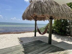 A beach with a thatched-roof structure, a hammock, and a wooden deck. - Charming Beach House directly ON the beach (Islamorada)