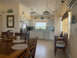 A kitchen with white cabinets, a dining table with chairs, a ceiling fan, and a window with curtains. - Charming Beach House directly ON the beach (Islamorada)