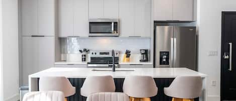 Una cocina moderna con una isla central, electrodomésticos de acero inoxidable y taburetes de bar.