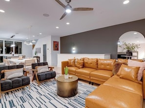 A modern living room with a sectional sofa, a round coffee table, and a ceiling fan. - Skyline Stunner | 4BR • 11 Beds • 2 Miles to DT! (Nashville)