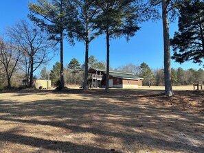 A two-story building with a green roof, surrounded by tall trees and a grassy field.
