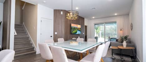 Un comedor moderno con una mesa de vidrio, sillas tapizadas blancas y una lámpara colgante.