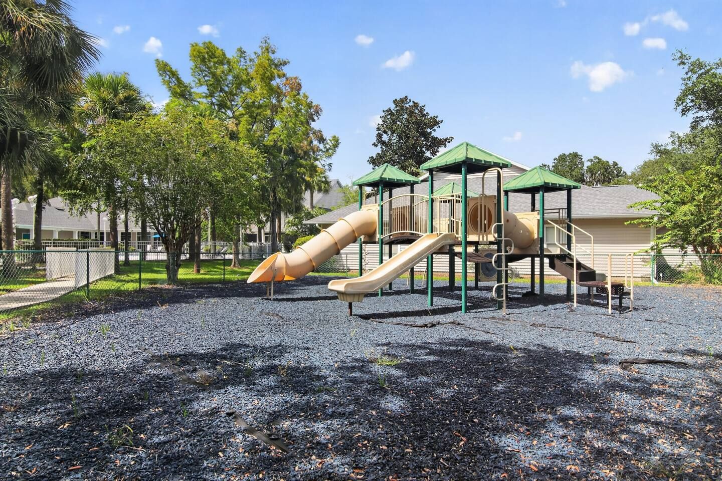 Ein Spielplatz mit Rutsche und Klettergerüsten, umgeben von Bäumen und einem Gebäude im Hintergrund.