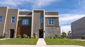 A modern multi-story residential building with a central entrance, a covered garage, and a stone accent wall. - New Doppio Home · Pool · 15min to Disney (Davenport)