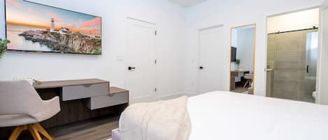 Un dormitorio moderno con cama, escritorio, silla y un cuadro de una escena costera.