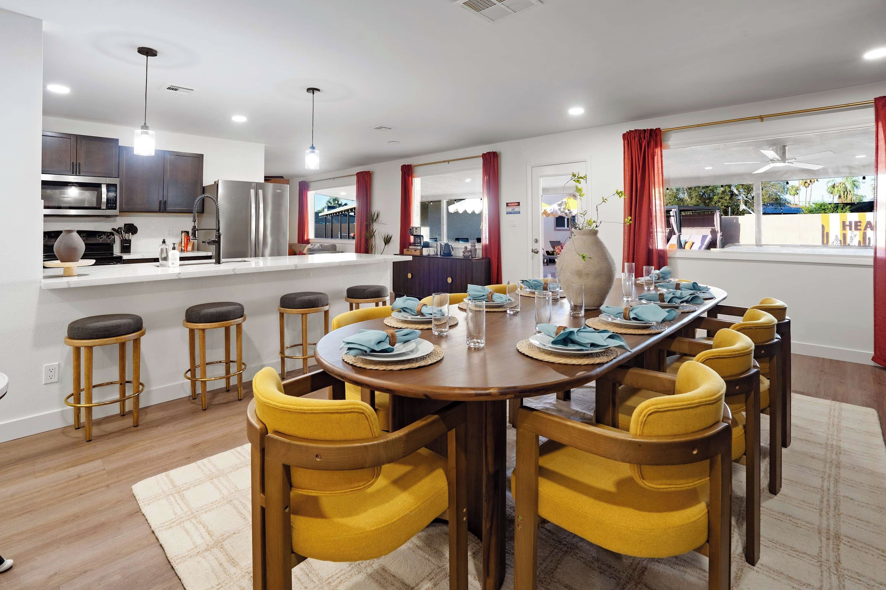 A modern kitchen with stainless steel appliances, a dining area with yellow chairs, and a view of the outdoors.