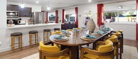 A modern kitchen with stainless steel appliances, a dining area with yellow chairs, and a view of the outdoors.