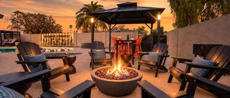 An outdoor seating area with a fire pit, lounge chairs, and a covered patio.
