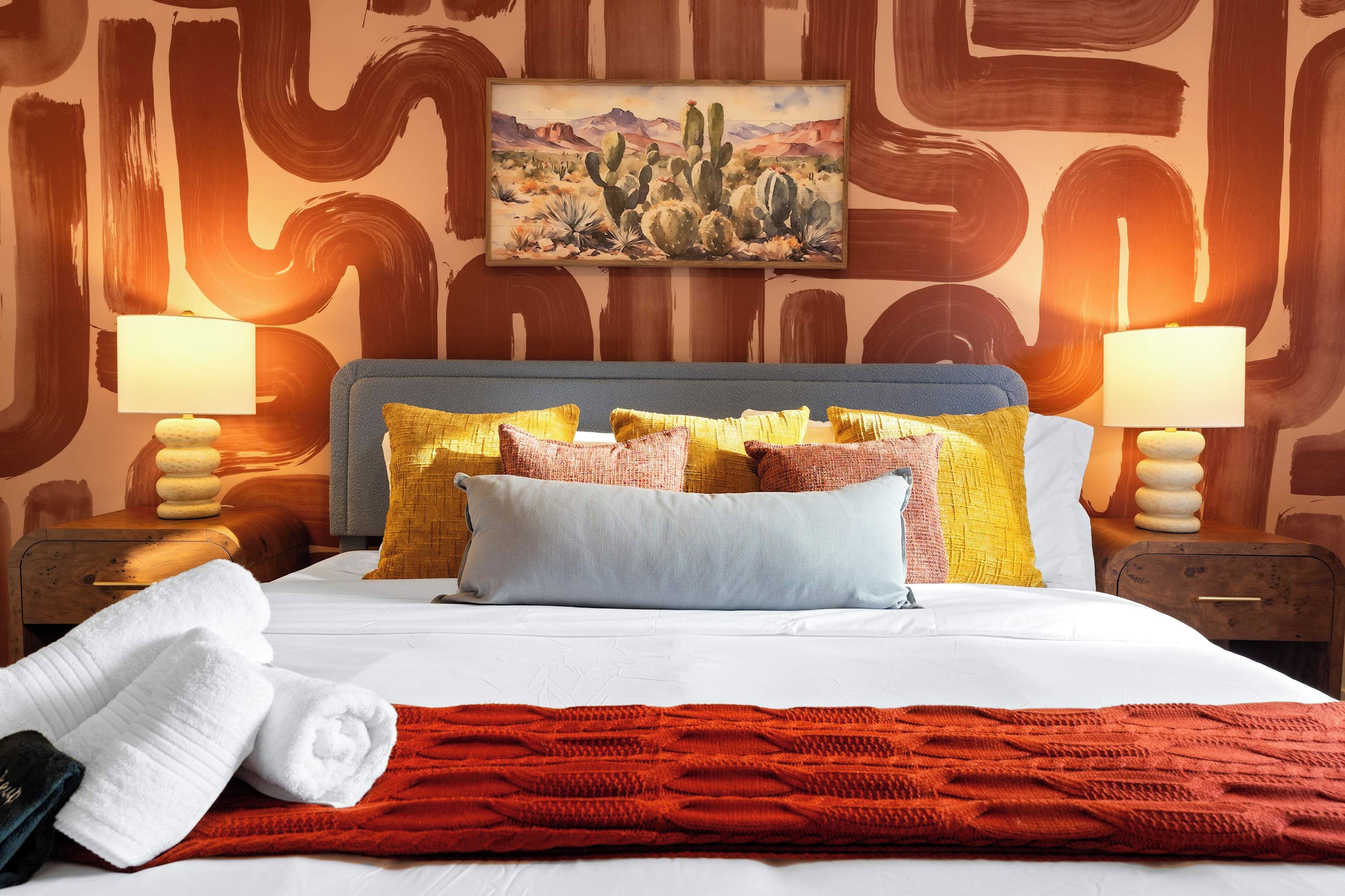 Una habitación de hotel con una cama, almohadas, una manta, un cuadro y dos lámparas.