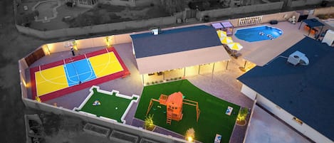 Vue aérienne d’un complexe sportif comprenant un terrain de basketball, une piscine et un espace de jeux pour enfants.