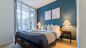 A bedroom with a bed, two bedside lamps, a window, and a view of the outside.