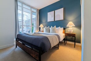A bedroom with a bed, two bedside lamps, a window, and a view of the outside.