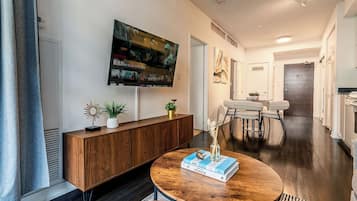 A modern living room with a round wooden coffee table, a mounted TV, and a dining area with a white table and chairs.