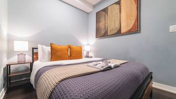 A bedroom with a bed, two bedside tables with lamps, a large abstract painting on the wall, and a magazine on the bed.
