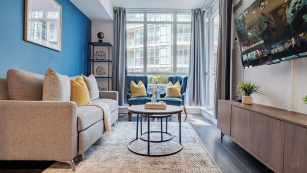 A modern living room with a sofa, armchairs, a coffee table, and a flat-screen TV mounted on the wall.