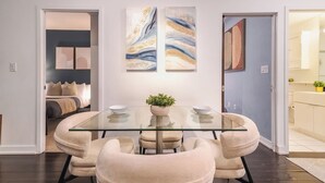 A dining area with a glass table, beige chairs, and two abstract paintings on the wall.