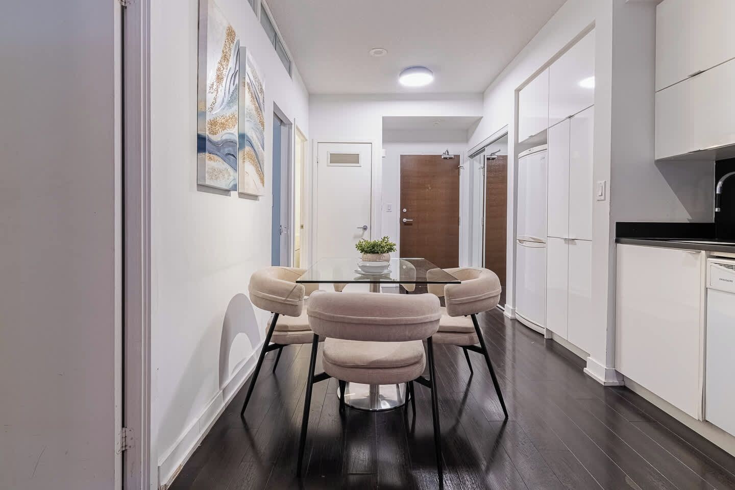 A modern kitchen with white cabinets, a black countertop, and a dining area with a glass table and cushioned chairs.