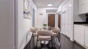 A modern kitchen with white cabinets, a black countertop, and a dining area with a glass table and cushioned chairs.