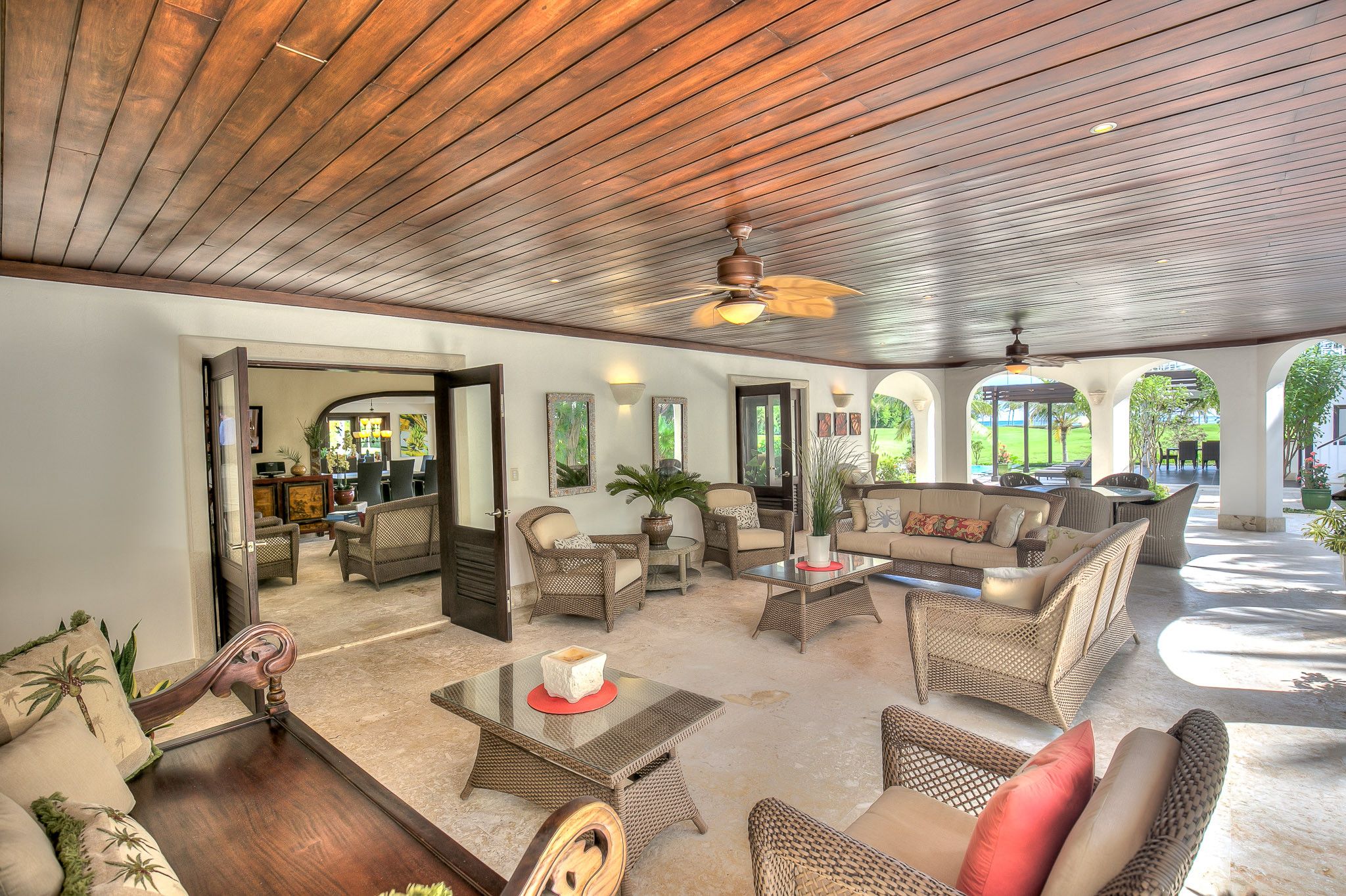 A spacious indoor area with wicker furniture, a ceiling fan, and a view of the outdoors.