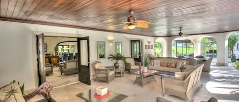A spacious indoor area with wicker furniture, a ceiling fan, and a view of the outdoors.