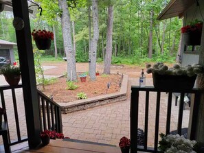 A wooden deck with a view of a landscaped garden area, a small pond, and a wooden cabin in the background.