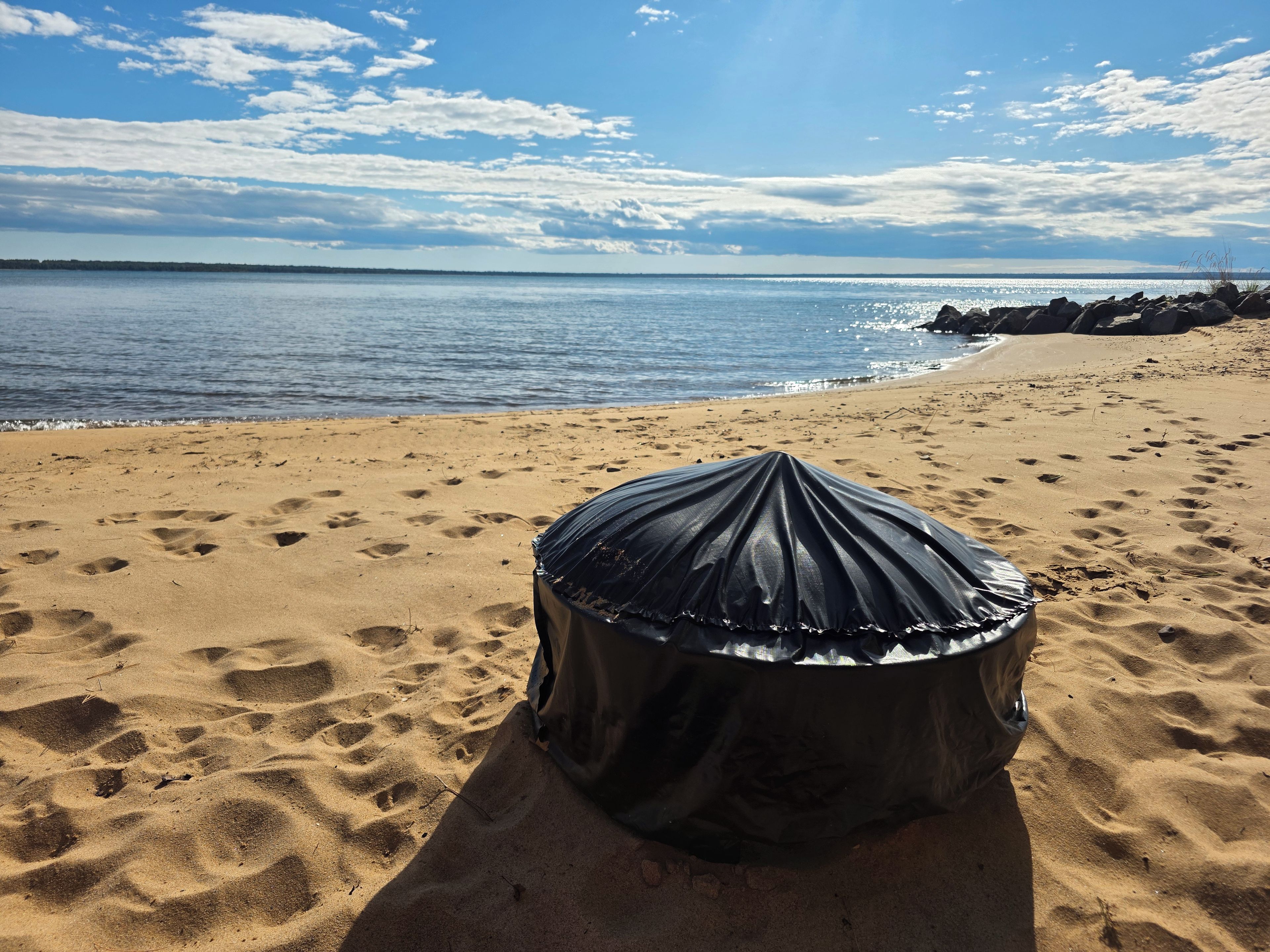 A beach with a black object on the sand, a clear sky, and the ocean in the background.