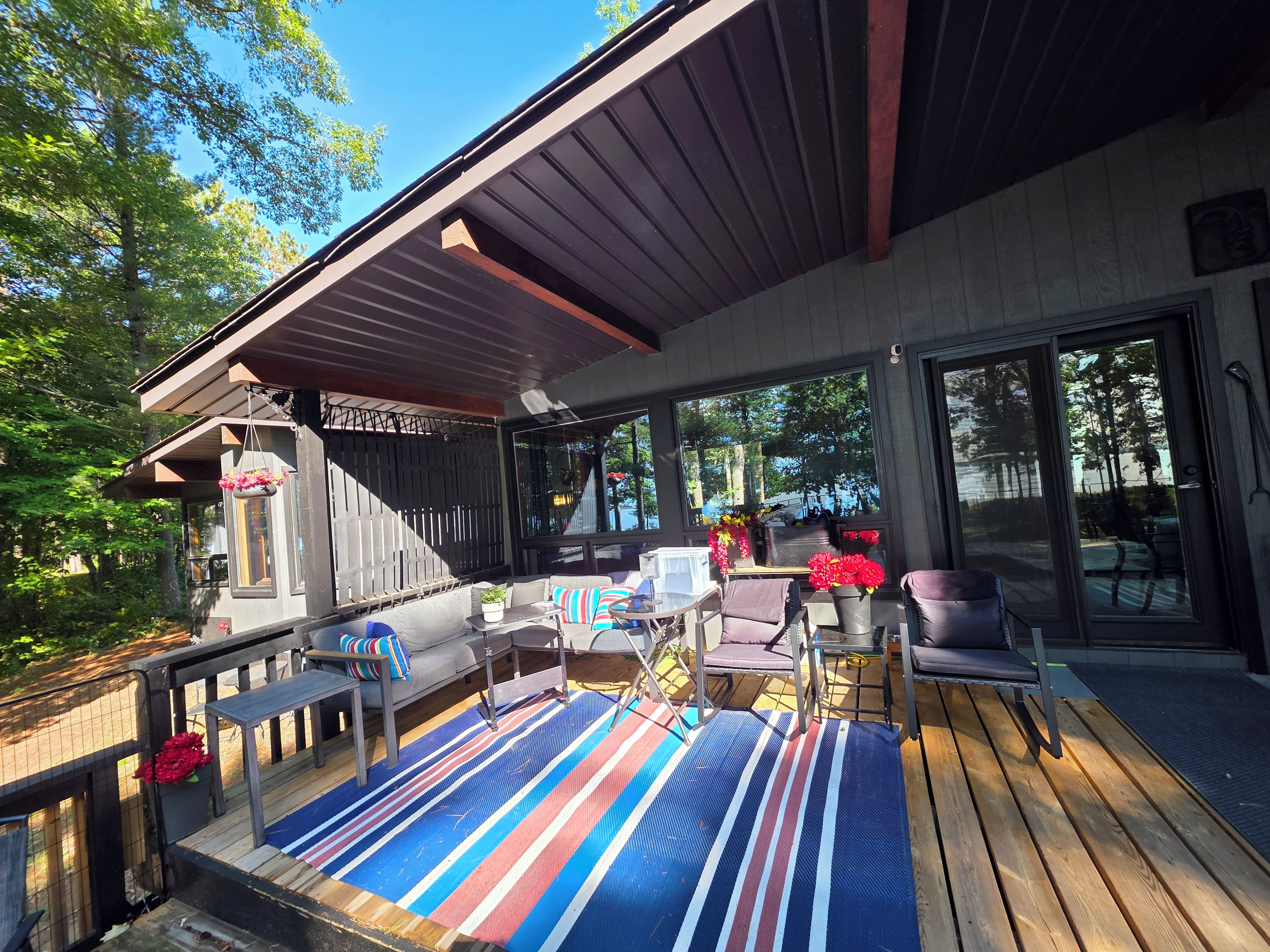 A covered outdoor seating area with a sofa, chairs, and a table, overlooking a forested area.