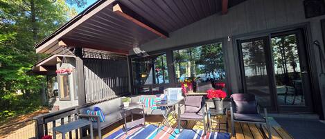 A covered outdoor seating area with a sofa, chairs, and a table, overlooking a forested area.