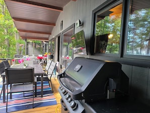 Une terrasse extérieure équipée d’un barbecue, d’un espace salon et de grandes fenêtres.