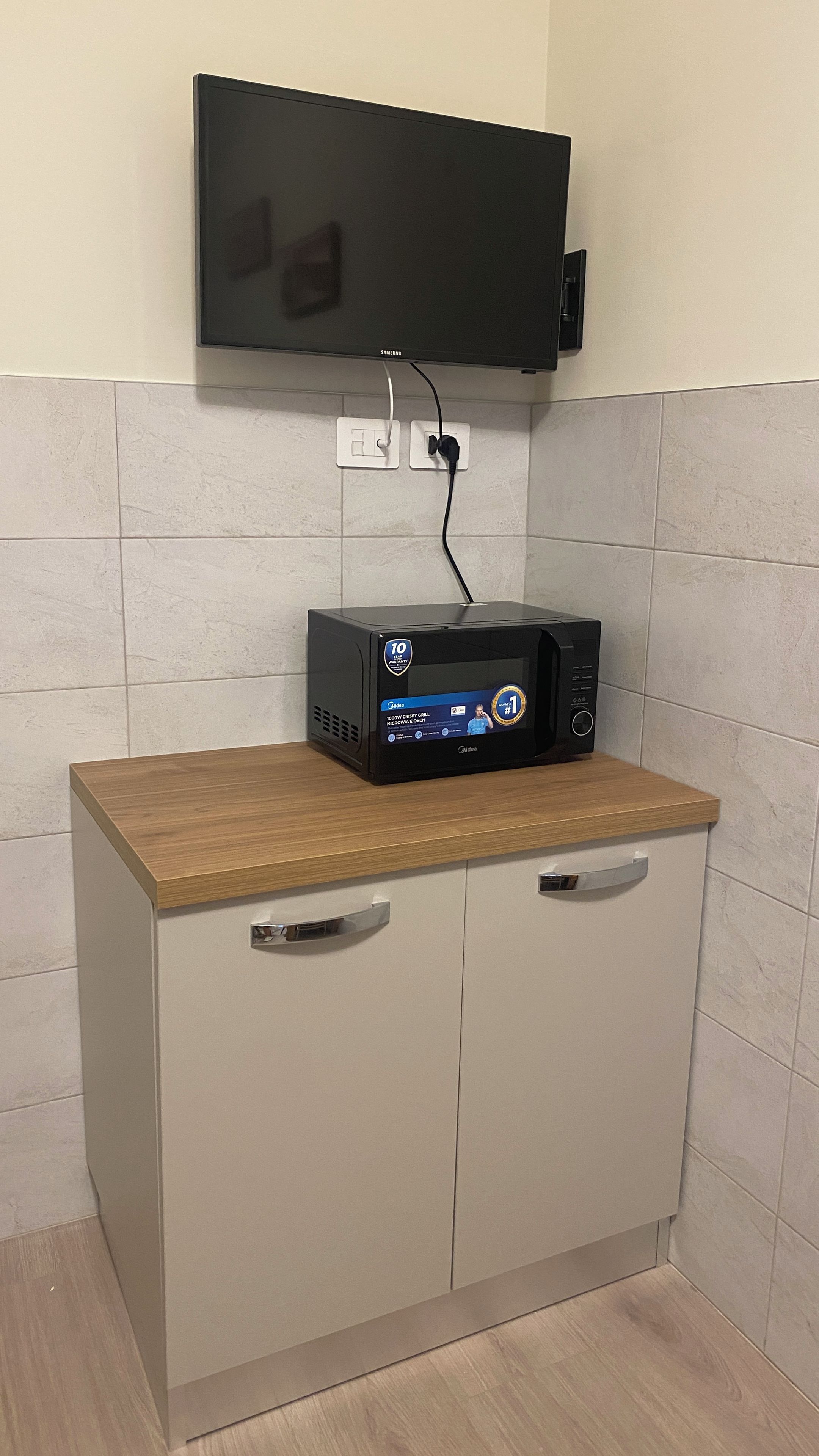 A microwave oven on a cabinet with a television mounted above it.
