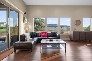 Amplia sala de estar con sofá seccional, una mesa de centro y grandes ventanales con vistas al exterior.