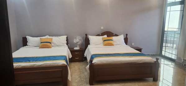 A hotel room with two beds, a nightstand, a fan, and a window.