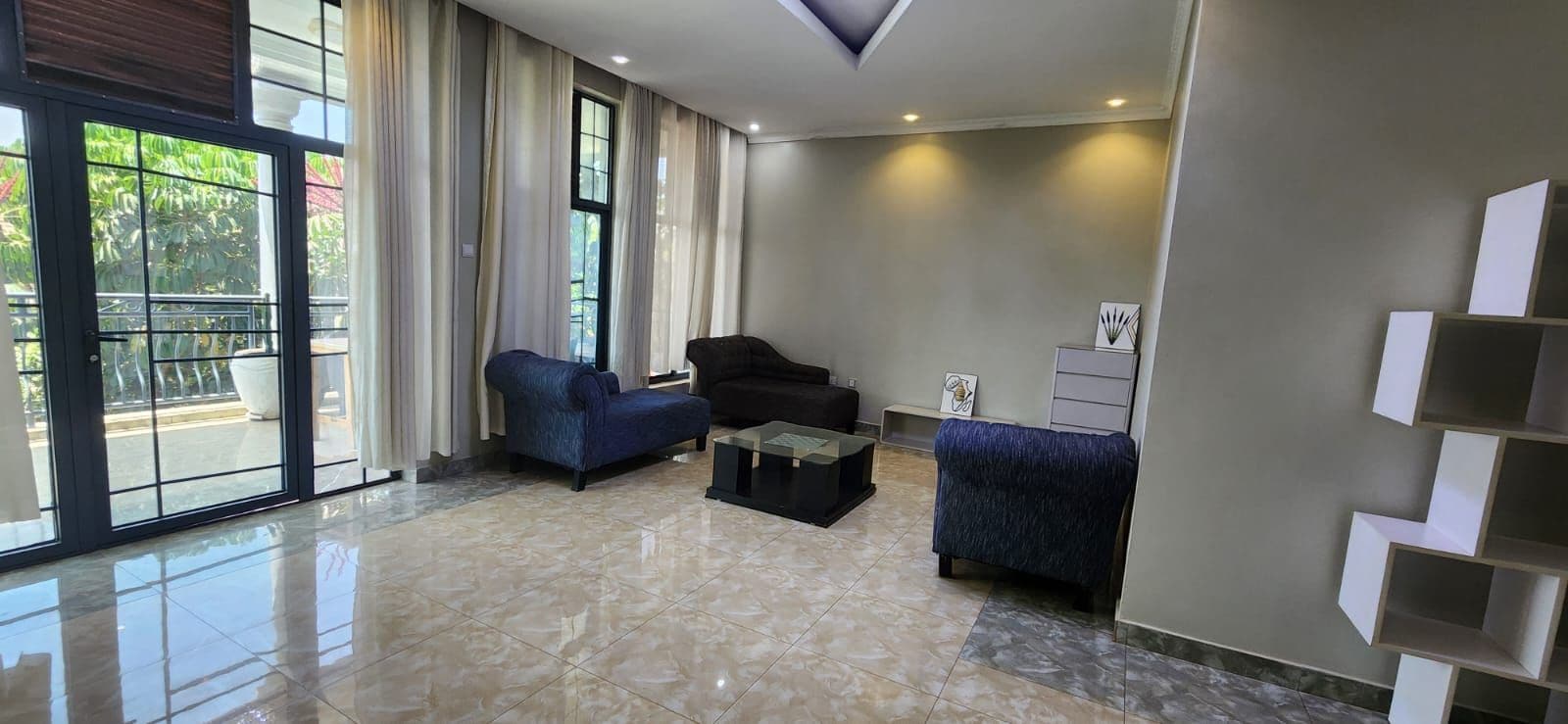 Una sala de estar moderna con un gran ventanal corredero, un sofá, una mesa de centro y una estantería decorativa.
