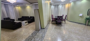 A hotel room with a seating area, a dining table with chairs, a small white table, and a glass-top side table.