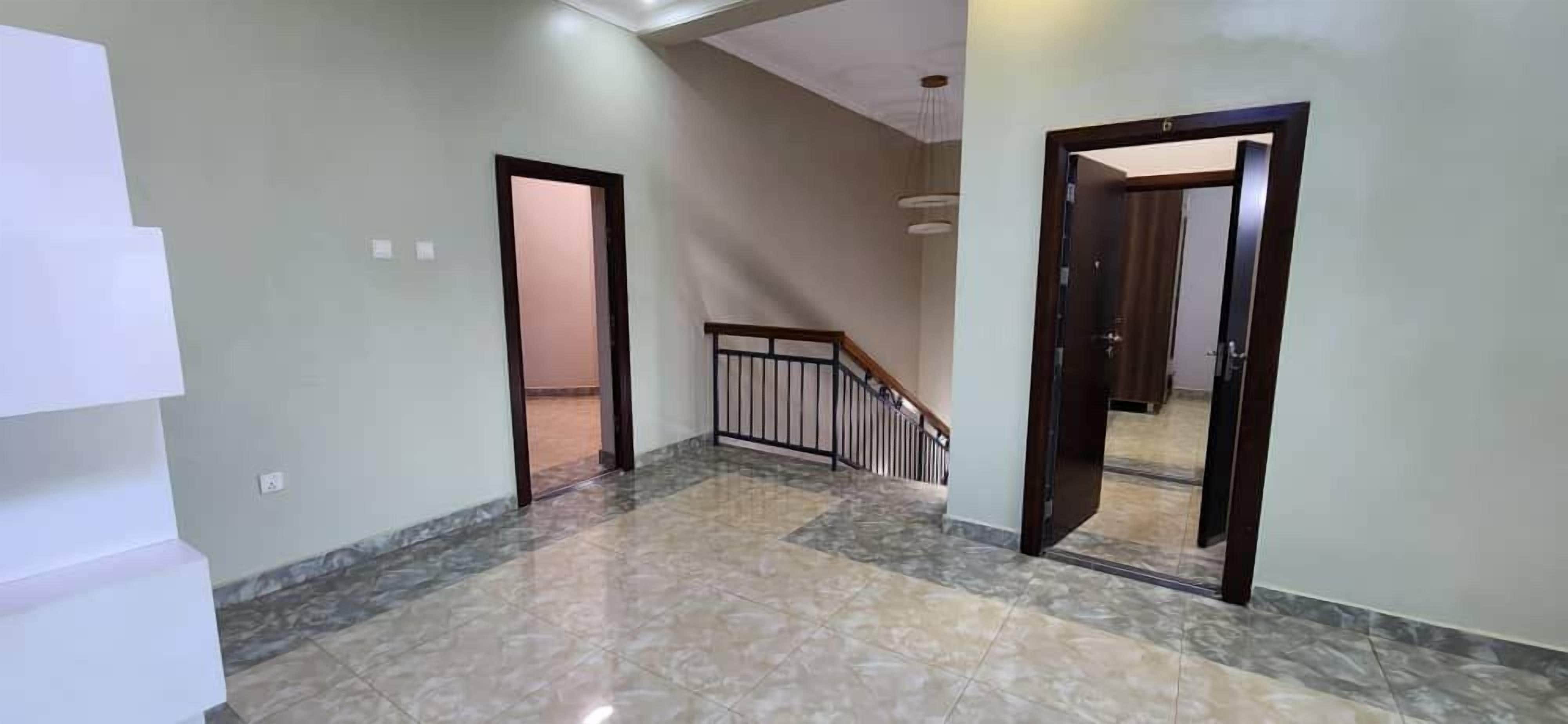 Ein Korridor mit Marmorboden, Holztüren und einer Treppe mit Metallgeländer.