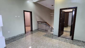 Un pasillo con piso de mármol, puertas de madera y una escalera con barandal de metal.