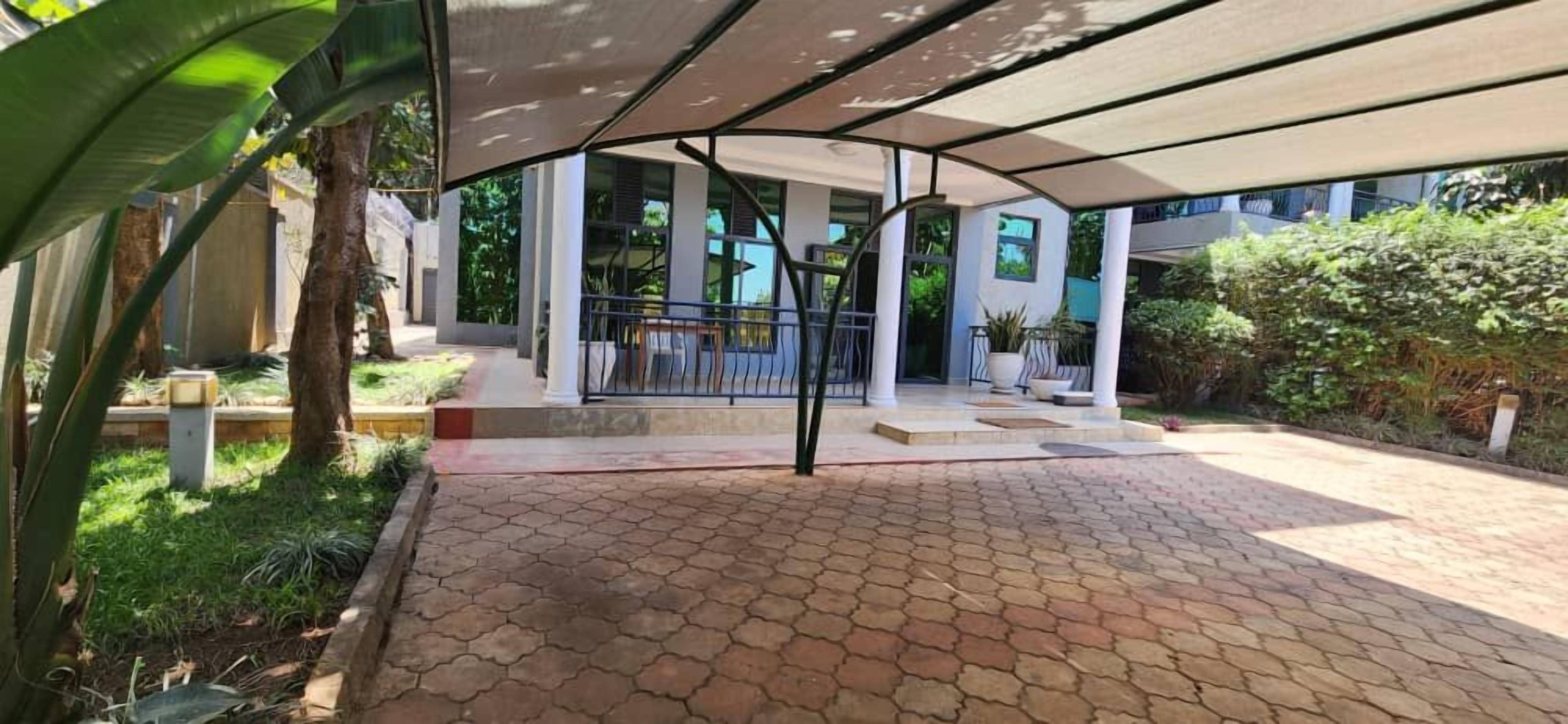 A covered outdoor area with a paved walkway, a staircase leading to a building entrance, and surrounding greenery.