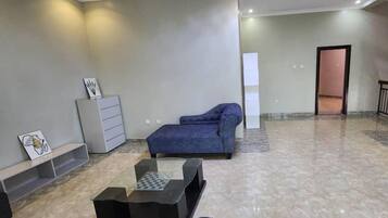 Una habitación amplia con un sofá azul, una mesita y un armario.