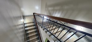 A staircase with a wooden handrail and metal balusters, leading to a landing with a light fixture.