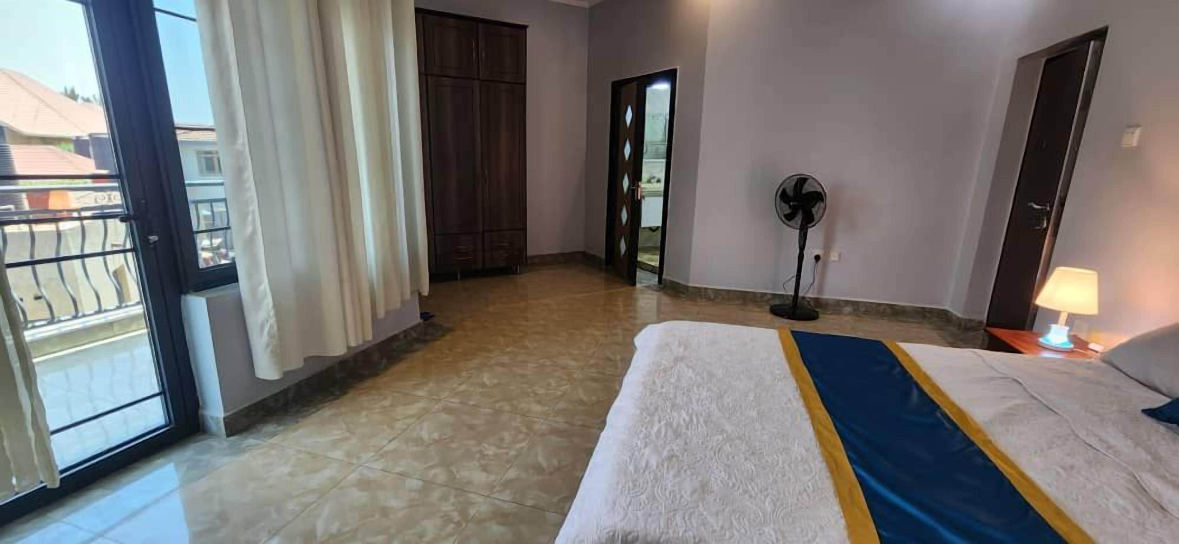Una habitación de hotel con cama, ventilador, lámpara y vistas al exterior.