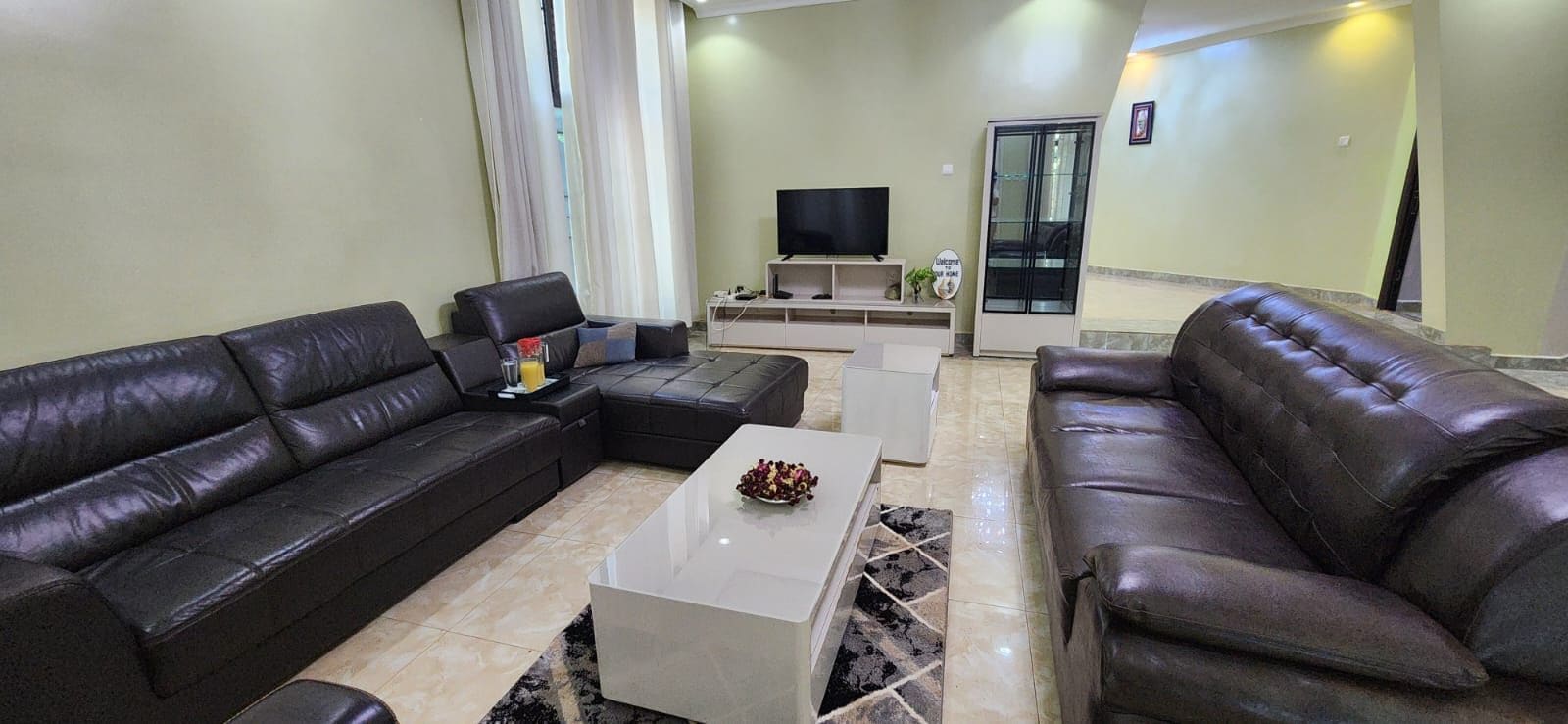 Una sala moderna con sofás de cuero, un televisor de pantalla plana y un aparador de vidrio.