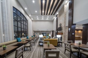 Um saguão de hotel com áreas de estar, mesas e uma grande janela.