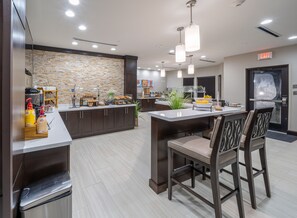 A modern kitchen with a stone backsplash, a buffet counter, and a seating area with bar stools.