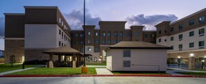 A multi-story hotel with a covered outdoor seating area, a fire lane, and a gated parking area.
