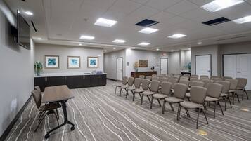 A conference room with a long table, chairs, a reception desk, framed artwork, and a television.