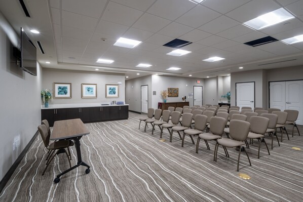 A conference room with a long table, chairs, a reception desk, framed artwork, and a television.