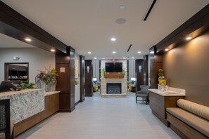 Um hall de hotel com uma receção, área de estar, lareira e uma televisão na parede.