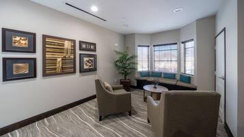 A hotel room with a seating area, framed artwork on the walls, and a potted plant.