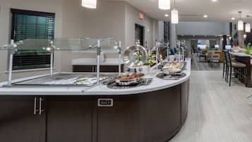 A buffet area with a variety of food options, a seating area with tables and chairs, and a modern design with pendant lighting.